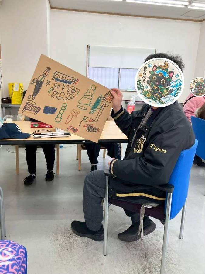 段ボールに描いた絵を見せるメンバーさん